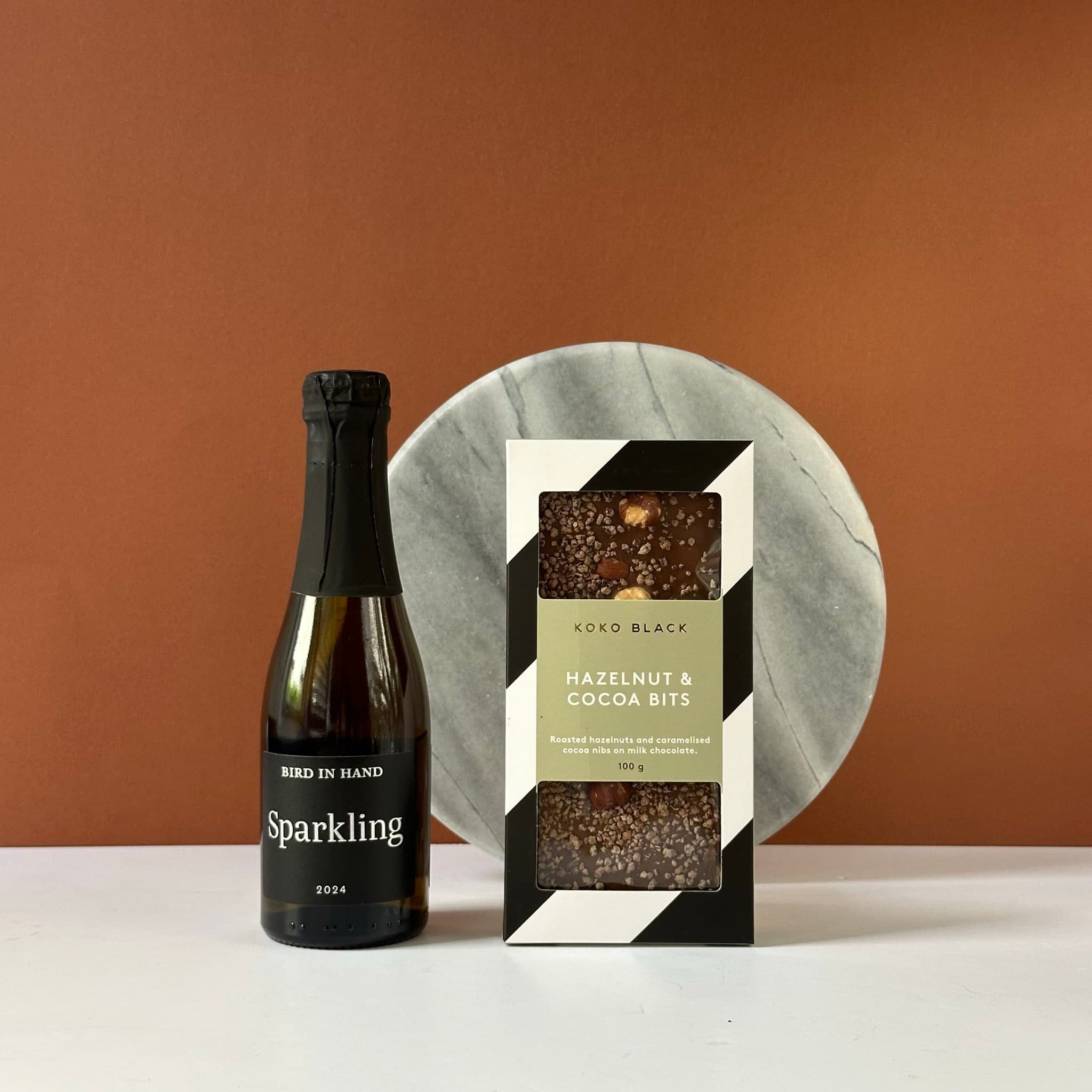 A festive gift bundle featuring a Bird in Hand Sparkling mini bottle and Koko Black Hazelnut & Cocoa Bits chocolates, elegantly packaged in a premium Thankly black box.