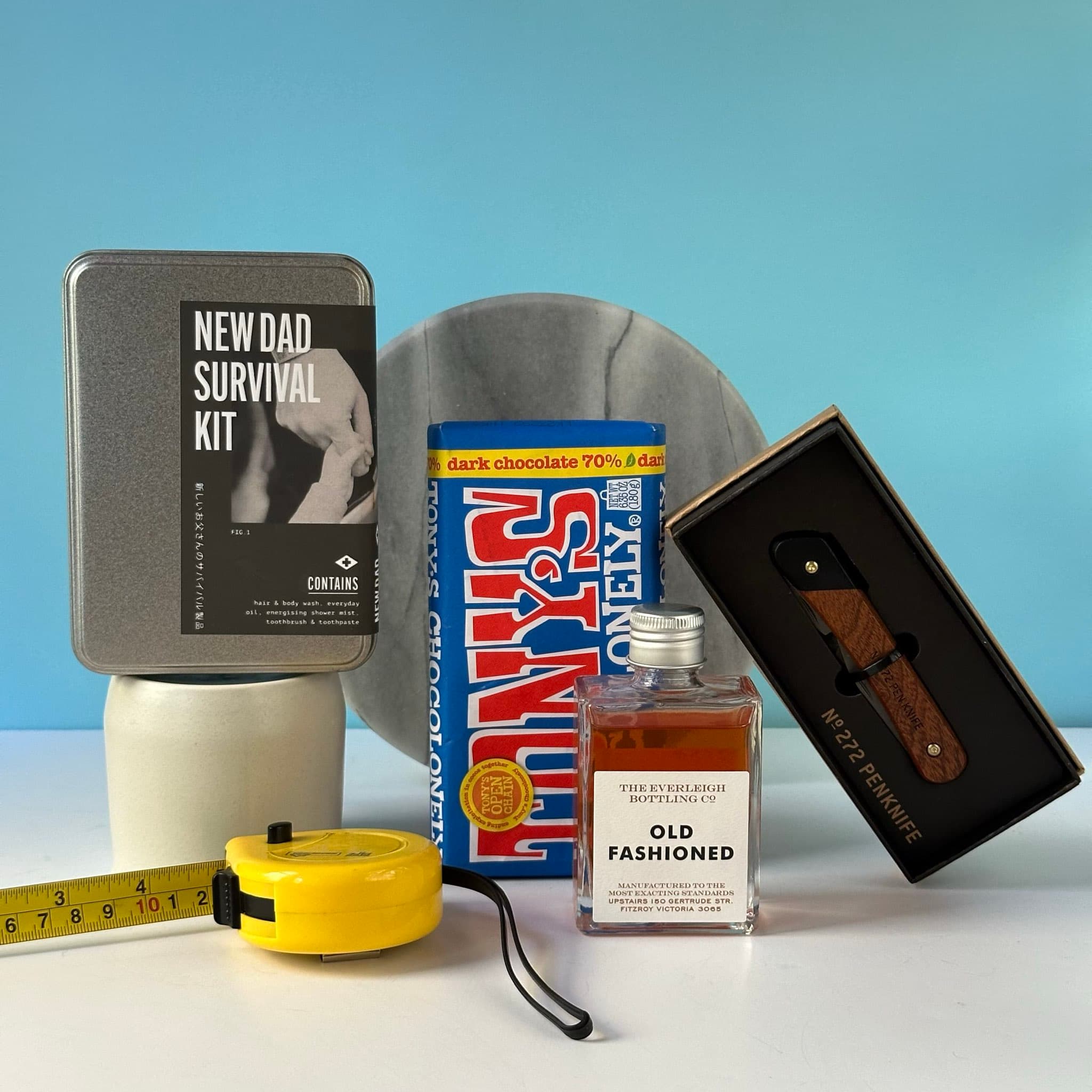 The New Dad Kit featuring an Old Fashioned cocktail bottle, Men's Society survival kit, multi-tool penknife, Tony’s Chocolonely dark chocolate, and a handwritten Thankly card, all packaged in a premium black box.