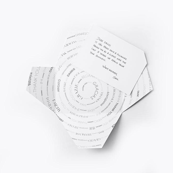 Signature Thankly Card with the Thank you envelope. Thank you is different languages written in a spiral pattern. Black font on a white background.